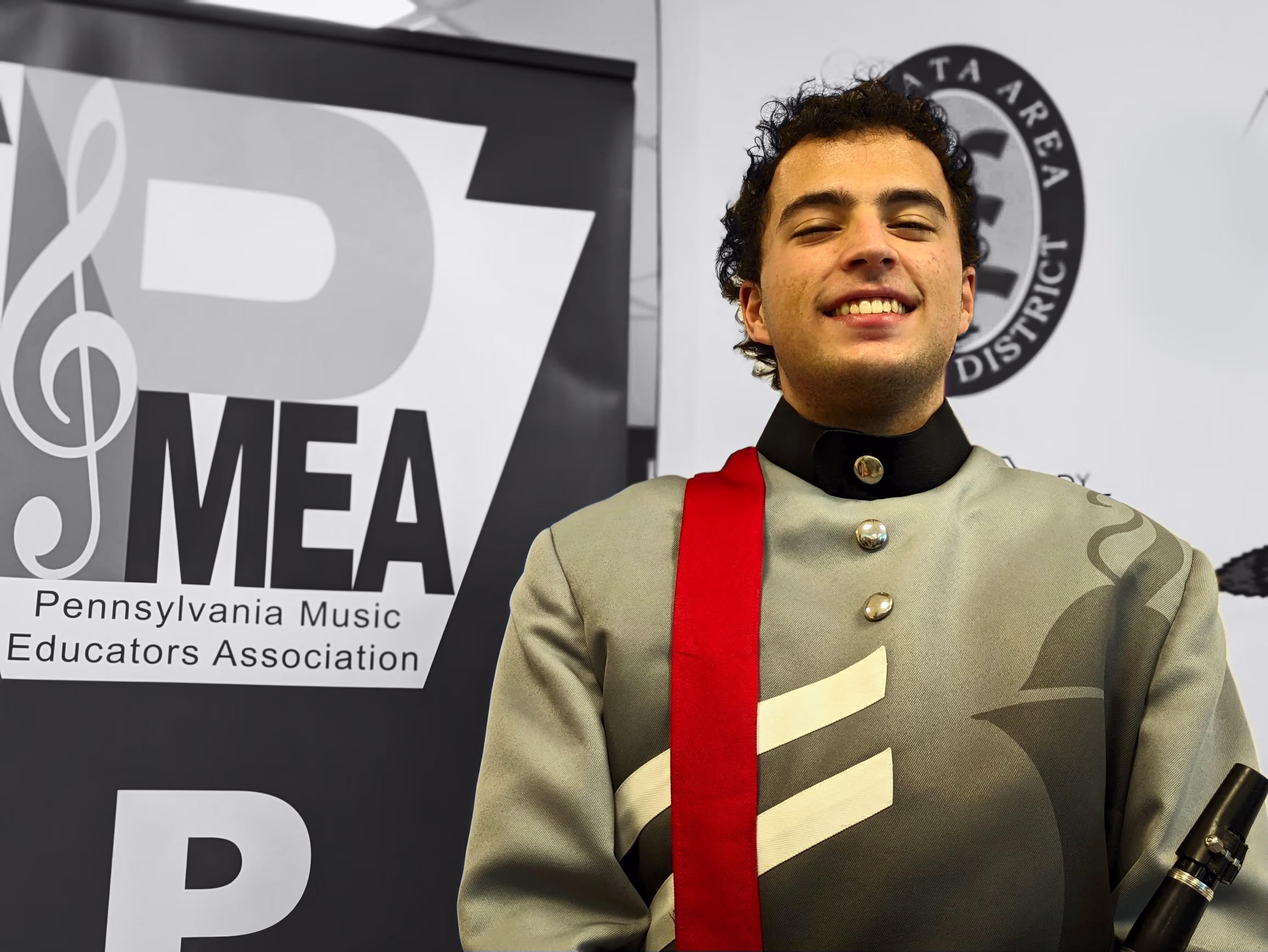 Photo of Andre in a band uniform standing next to a PMEA (Pennsylvania Music Educators Association) sign